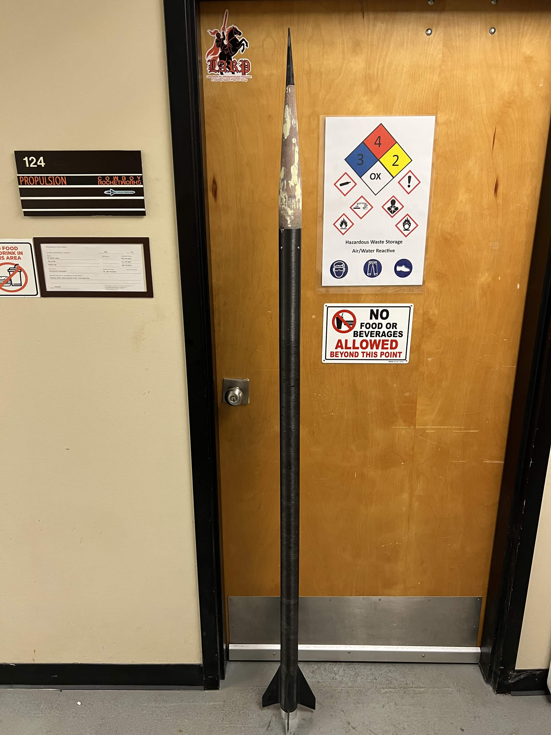 Invictus rocket standing upright in front of a propulsion laboratory door.
